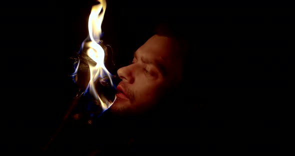 Closeup View of Male Face Illuminating Two Flaming Torches in Darkness, He Is Watching Flame