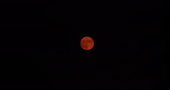 Time-lapse wide shot of a Harvest Moon as it slowly rises from the center the upper left. The color