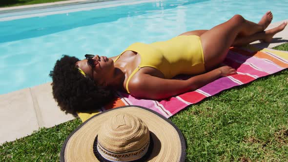 Mixed race woman lying on blanket sunbathing by the pool