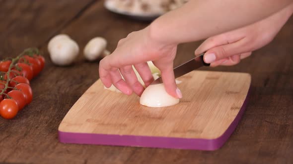 Chef's Hands with Knife Cutting the Onion on the Wooden Board.