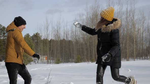 Young Couple is Having a Snowball Fight in Winter Forest