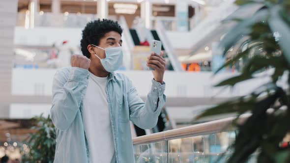 African Guy in Medical Face Protective Mask Stands in Mall Office Company Looking at Mobile Phone