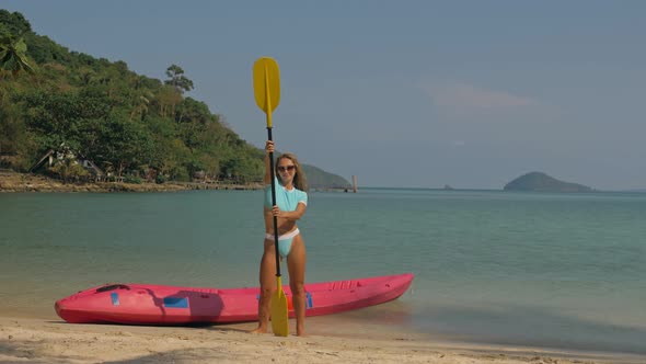 Pretty Young Sportswoman with Sunglasses and Swimsuit Holds Paddle Posing Near Pink Plastic Canoe on