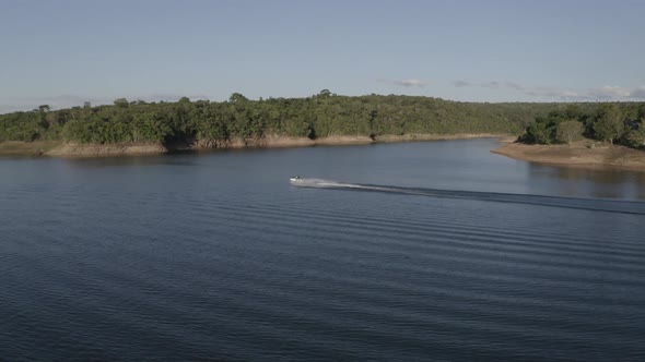 Person on a jet ski speeding along a large, idyllic lake along the tropical shoreline - aerial view