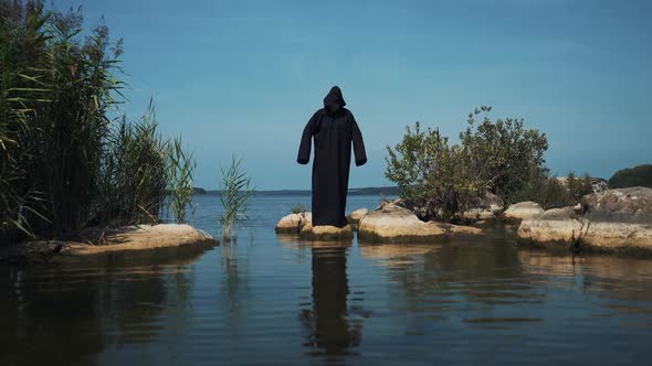 Terrible demon standing in the river. Scary figure in black mantle.
