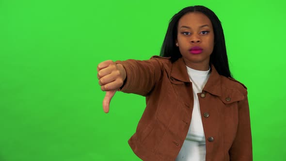 A Young Black Woman Shows a Thumb Down To the Camera - Green Screen Studio