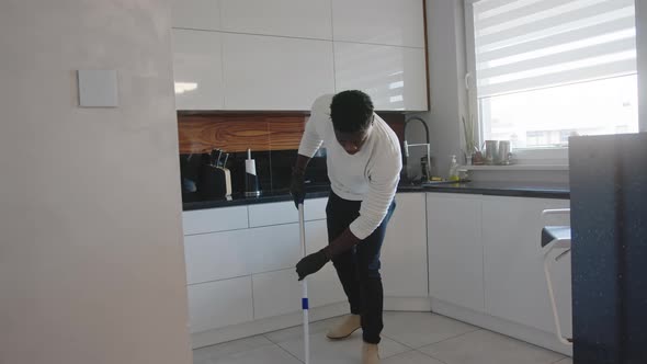 Happy Black Man Having Fun Dancing and Singing While Cleaning Floor in the Kitchen. Domestic Life