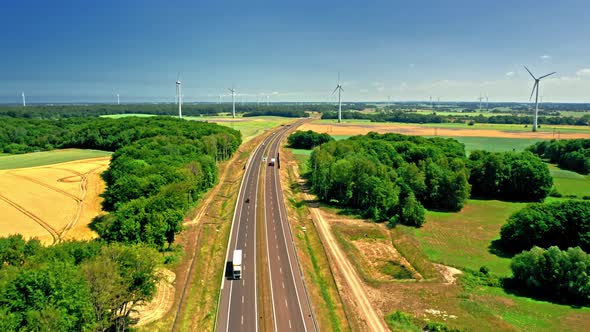 Aerial view of golden field and wind turbines near highway.