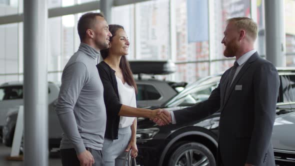 Happy Couple Shaking Hands with Salesman in Car Showroom