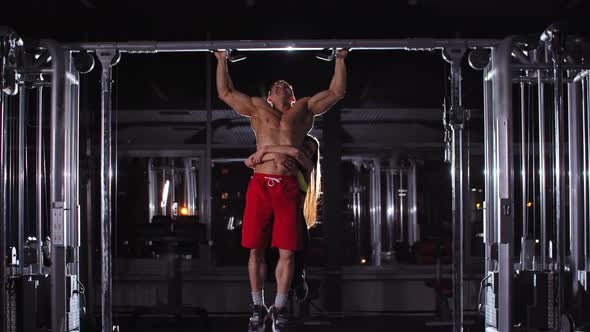 Man and Woman Training in the Gym  a Man Trying to Do Pull Ups with a Woman Hanging on His Waist