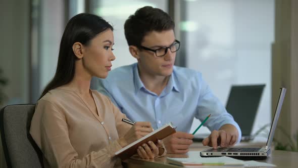 Experienced Male Employee Teaching New Colleague, Showing How to Use Application