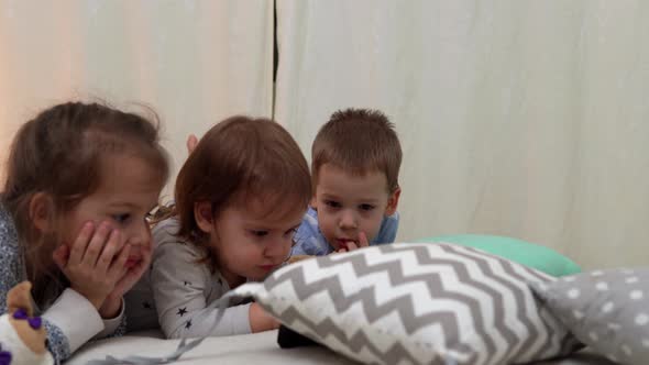 Smiling Preschool Toddler Children In Pajamas Watching Cartoon on Smartphone on Bed