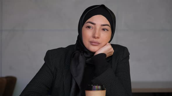 Young Muslim Woman in Hijab Drinking Tea or Coffee and Looking Away Thinking Solving Problem