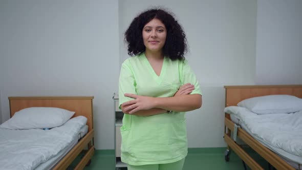 Confident Positive Nurse with Crossed Hands Smiling Looking at Camera Standing in Hospital Ward