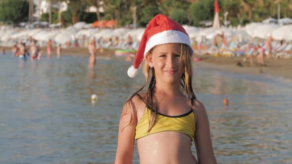 Little Adorable Girl in Red Santa Hat Having Fun at Beach.