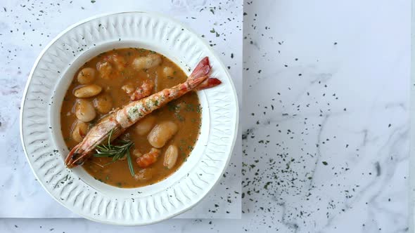 Bowl of delicious soup with seafood and white beans served on black table