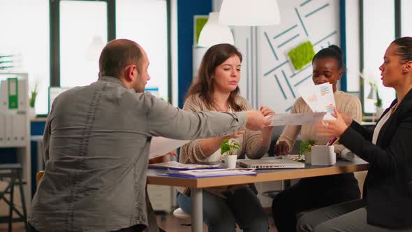 Young Diverse Team of Workers Talking Looking at Documents and Analyzing Graphs