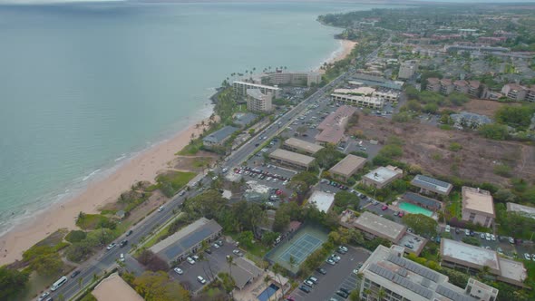 Drone footage tilting up, looking at tennis court, a beach, then a volcano in Hawaii.