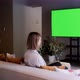A beautiful girl is sitting on a sofa in front of a TV with a green screen. Green screen TV. - VideoHive Item for Sale