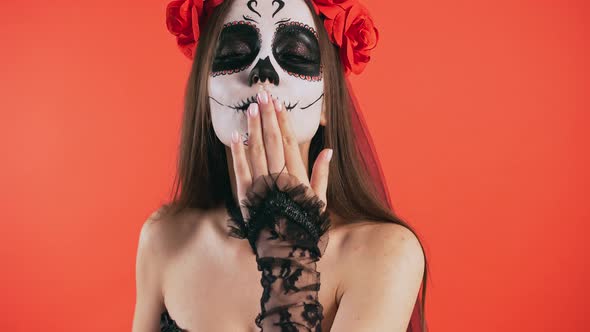 Day of Dead Lady with Sugar Skull Makeup Smiling and Sending you an Air Kiss Posing on Red