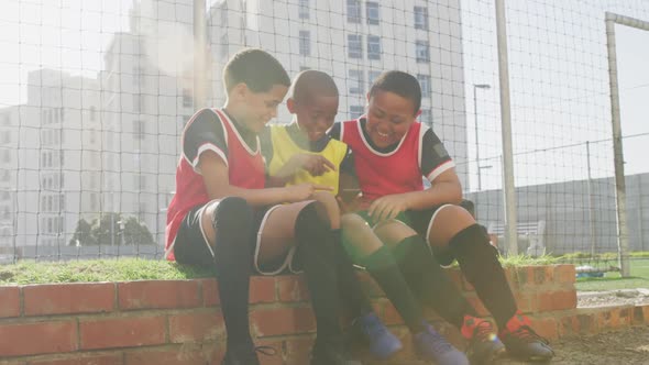 Soccer kids in red laughing and using a smartphone in a sunny day