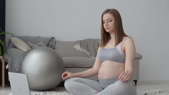 Pregnant Woman in Sportswear Sitting on the Carpet in the Lotus Position