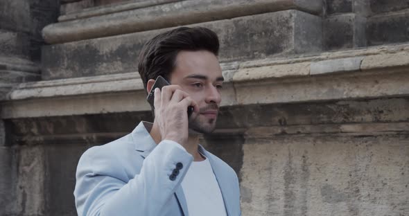 Young Man Rides Near The Ancient Castle In A Festive Light Suit And Talks On The Phone