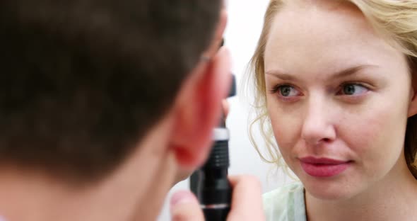 Optometrist examining female patient through ophthalmoscope