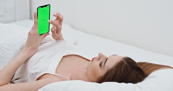 Young Girl Lying in Bed and Using Smartphone, Green Screen, Girl Is Resting Lying in Bed and Holding