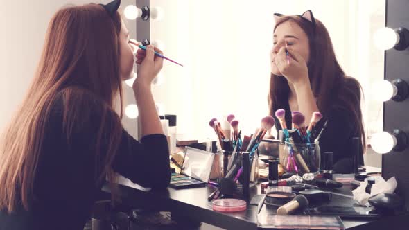 Young Woman Applying Makeup While Sitting at Her Vanity Table with Lots of Cosmetics