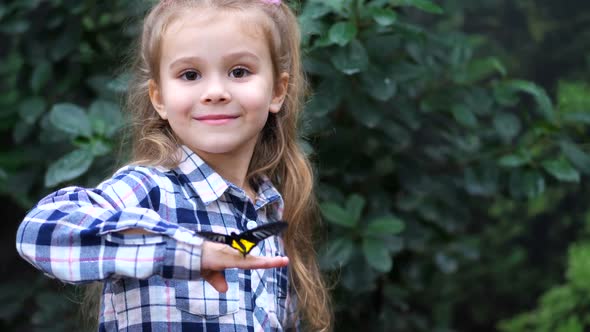A Very Cute Girl Holds a Butterfly on Her Hand Turns to Frame and Smiles
