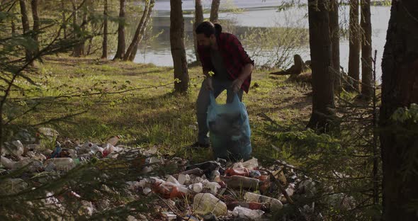 A Male Volunteer Collects Trash Scattered in the Forest in a Plastic Bag