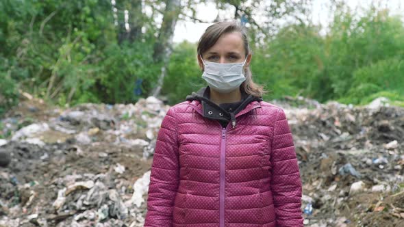 Woman in a Mask Standing Near the Garbage Pile