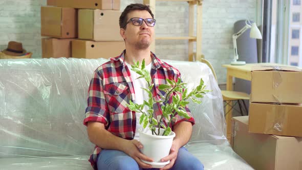 Disgruntled Man and a Flower Sitting on the Couch and Considering His New Modern Apartment