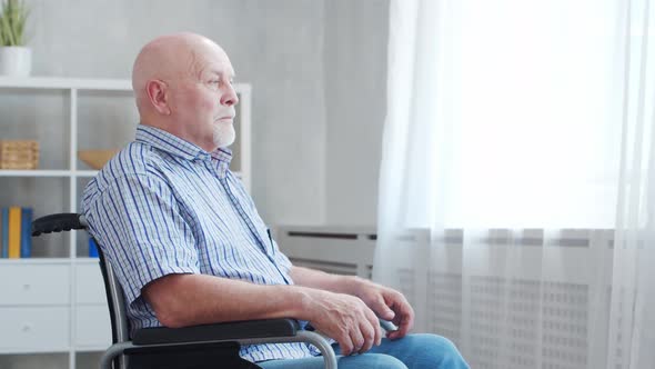 Disabled old man is sitting in a wheelchair at home alone. A handicapped person.