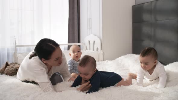 Affectionate Asian Mom Relaxing with Triplets in Bedroom