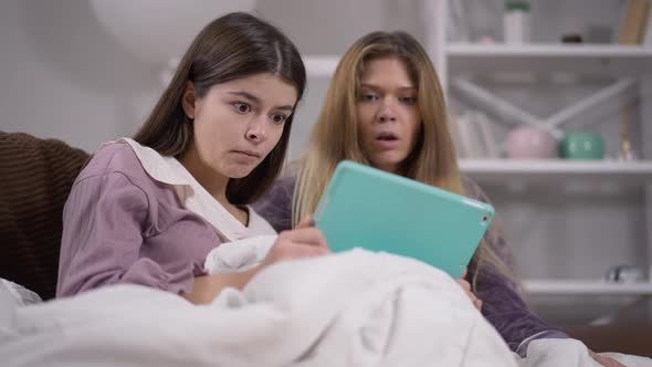 Scared Young Women with Frightened Facial Expression Watching Horror Movie Online on Tablet at