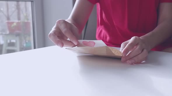 A Woman in a Red Dress Opens a Red Heartshaped Valentine's Delivered Envelope for Valentine's Day