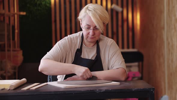 An Eldery Woman Flattening a Thin Piece of Clay