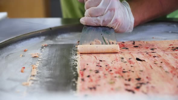 Worker carefully pushes up rolls of Thai rolled ice cream, slow motion close up 4K