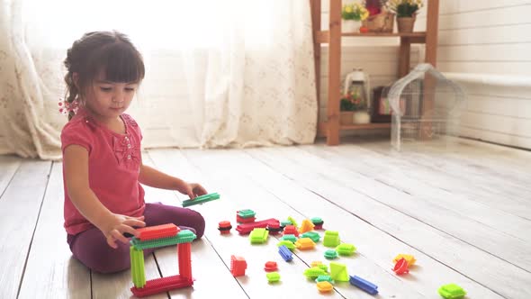 Little Beautiful Girl Sits on the Floor in the Room and Plays with a Colorful Constructor