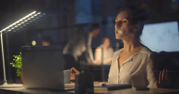 Businesswoman Relaxing and Meditating Sitting at Workplace in Modern Office at Night