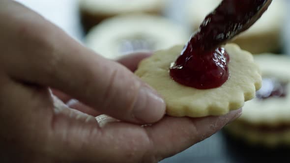 Woman filling Christmas cookies with jam