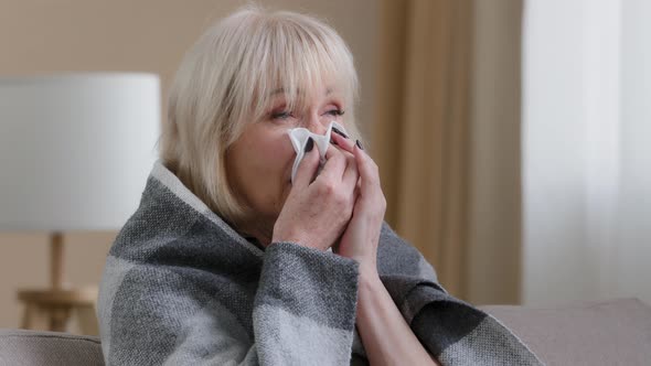 Close Up Ill Sick Old Blonde Grandmother 60s Woman Covered in Warm Blanket at Home Blowing Nose to