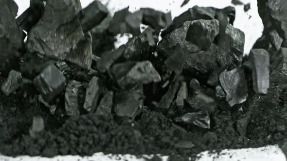 Super Slow Motion Shot of Coal Falling Into Black Powder on White Background at 1000 Fps