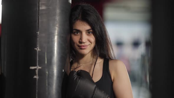 Confident Smiling Middle Eastern Sportswoman Looking at Camera Kicking Punching Bag