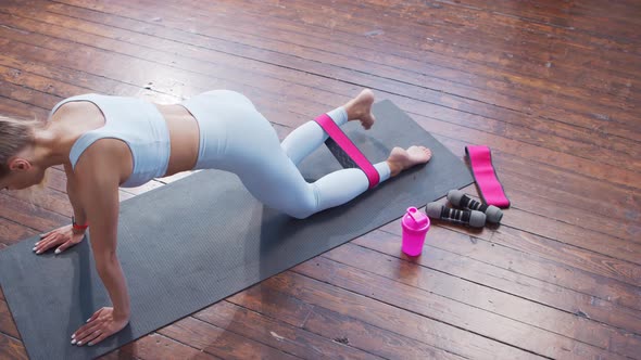 Young and sporty girl in sportswear is using resistance band while doing at home.