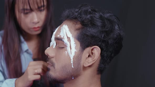 Professional make up artist putting white insert on man's face to make a scary Halloween mask