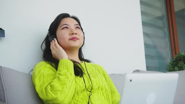 Young Asian Woman Listening To the Music From the Laptop Using Headphones