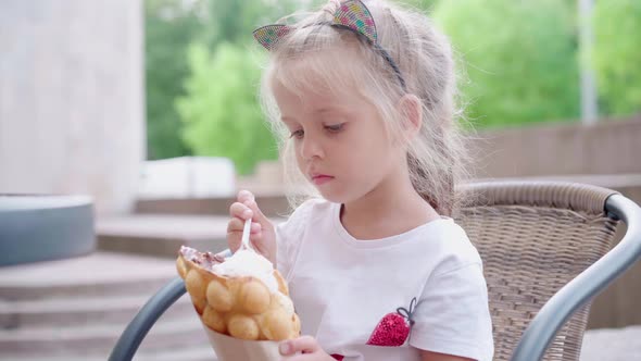 Little Girl Eat Bubble Waffle with Ice Cream Sitting Outdoor Cafe Summer Day